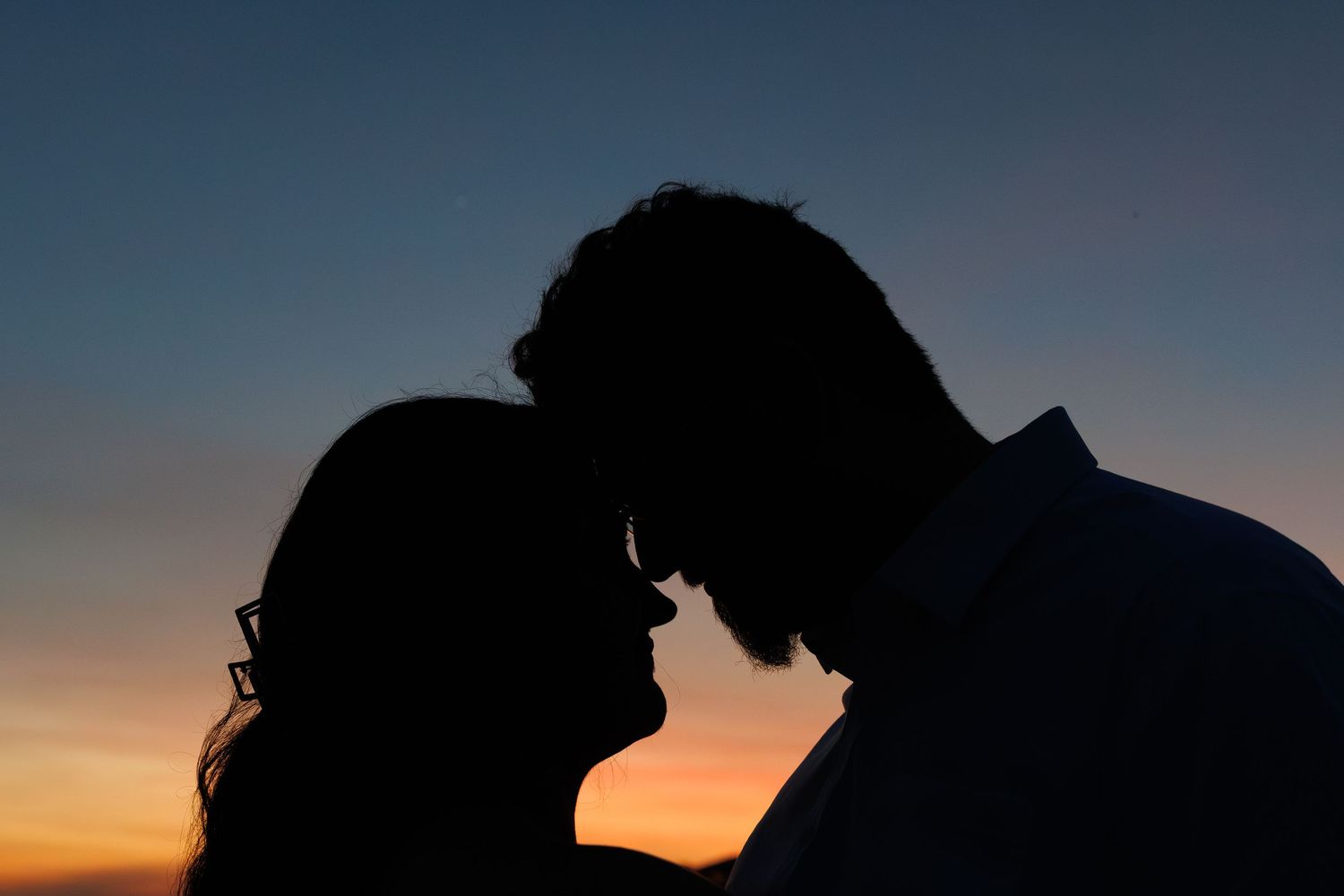 Romantic silhouette of a couple touching foreheads against a vibrant sunset sky.