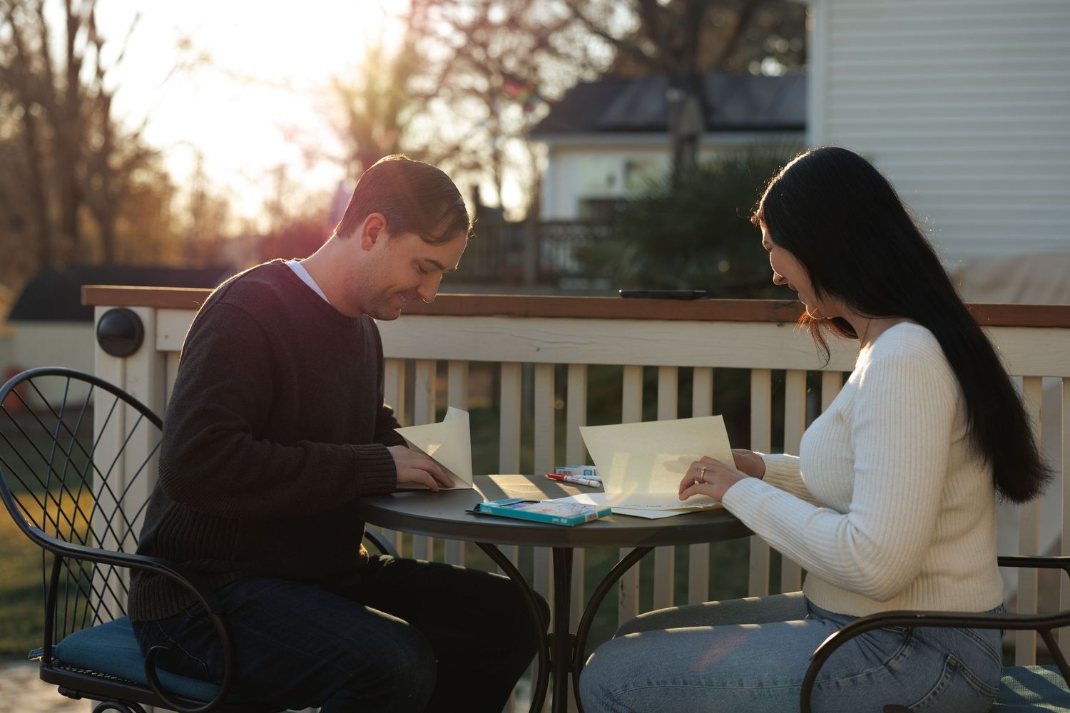 Couple sitting outdoors at a table reading cards together in warm golden sunset light.