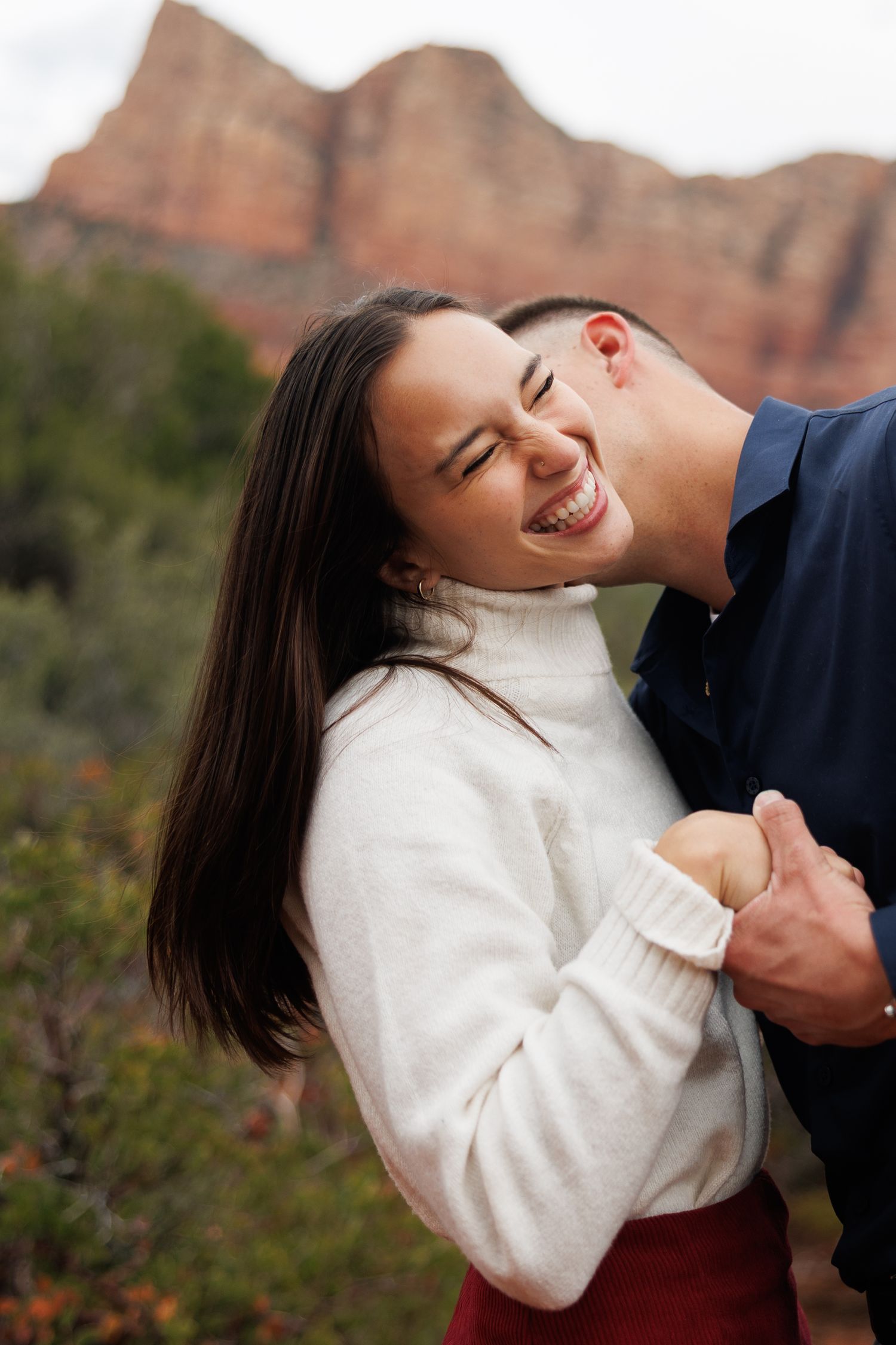 Couple laughing and embracing in front of red rock formations in Sedona, Arizona.