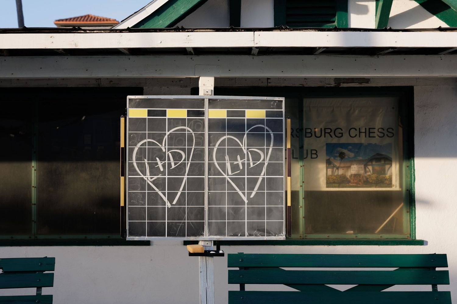 Two hearts with initials drawn on a chalkboard sign outside a chess club building.