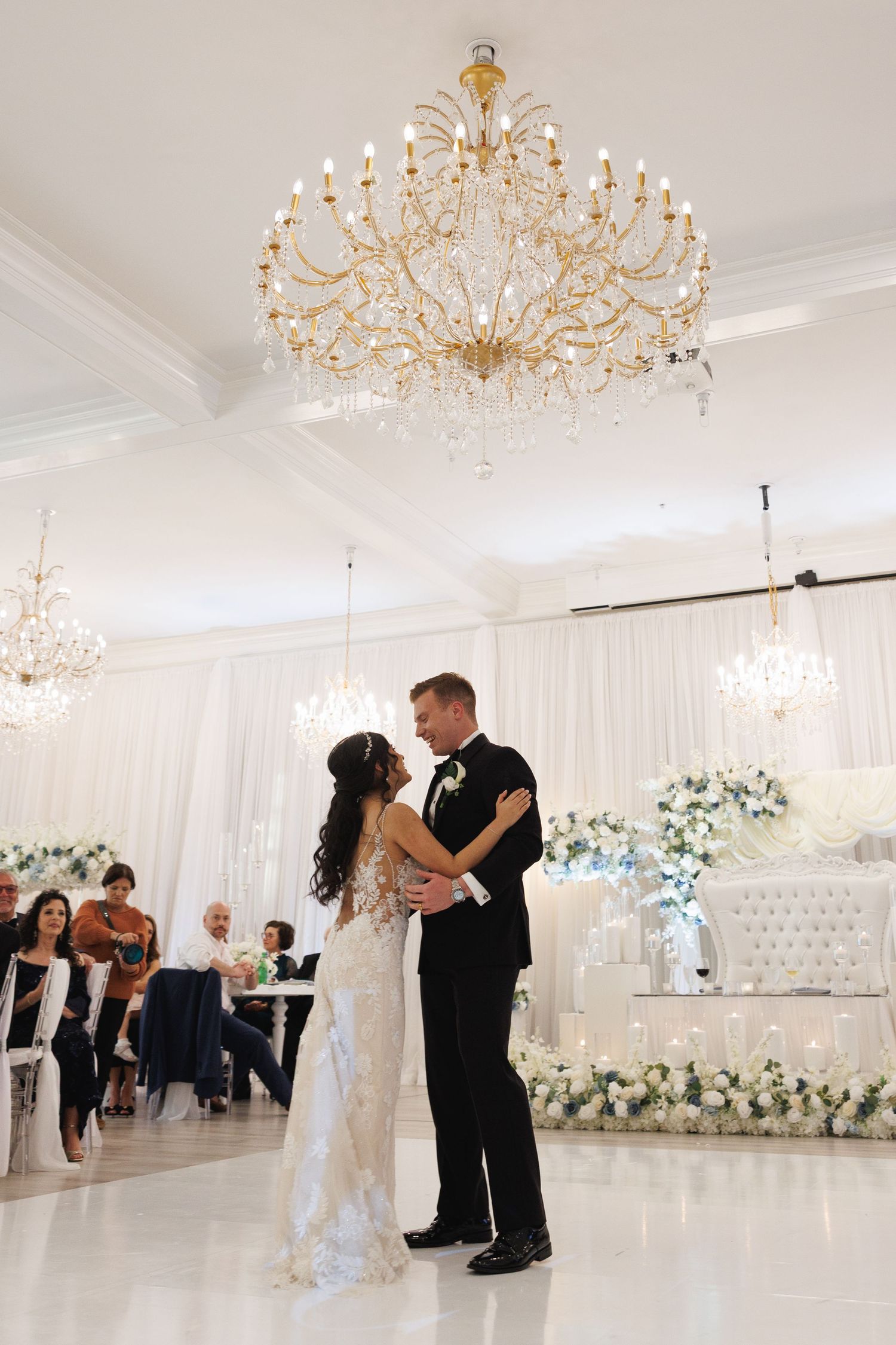 Bride and groom share their first dance beneath a gold crystal chandelier in an elegant white ballroom at The Yorkmont in Charlotte, NC.