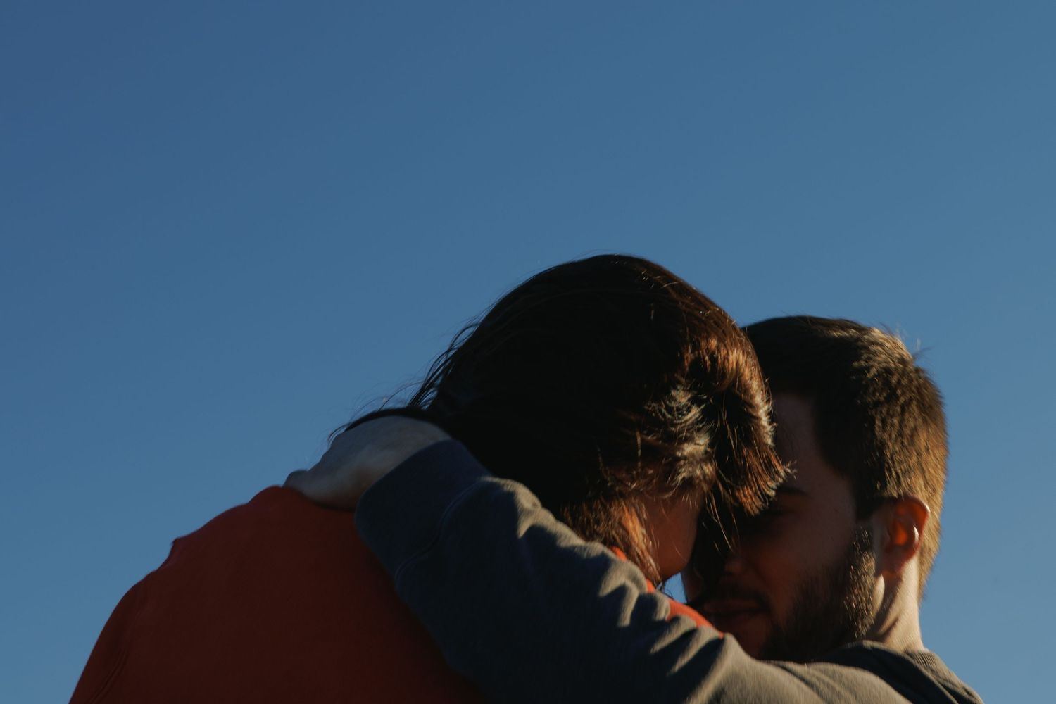 Couple sharing a tender embrace against a clear blue sky at dusk, romantic outdoor moment.