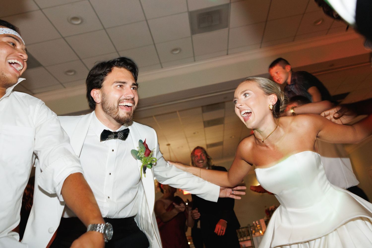 Joyful bride and groom dancing energetically with guests at lively wedding reception party.