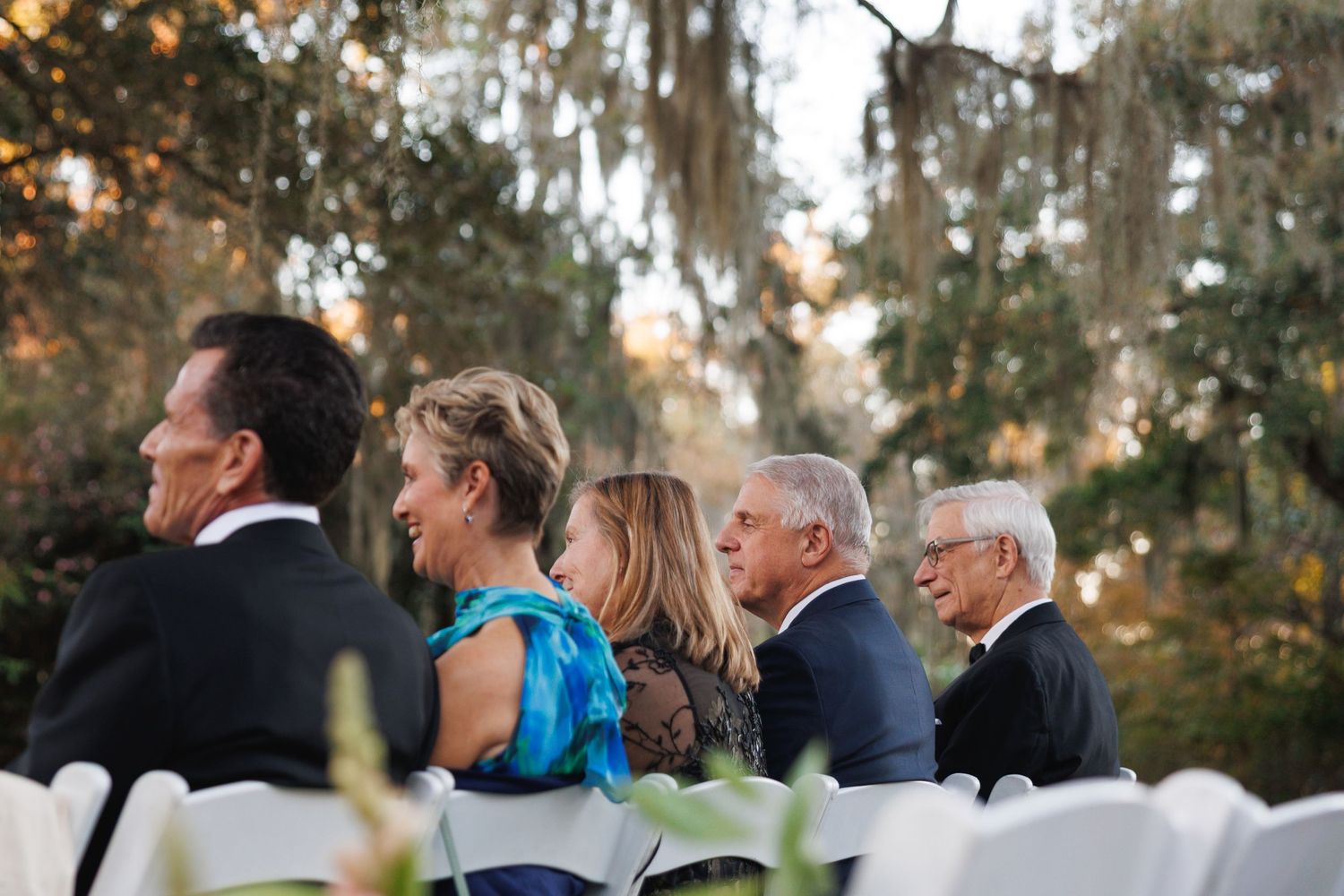 Wedding guests seated outdoors under Spanish moss-draped trees during elegant garden ceremony.