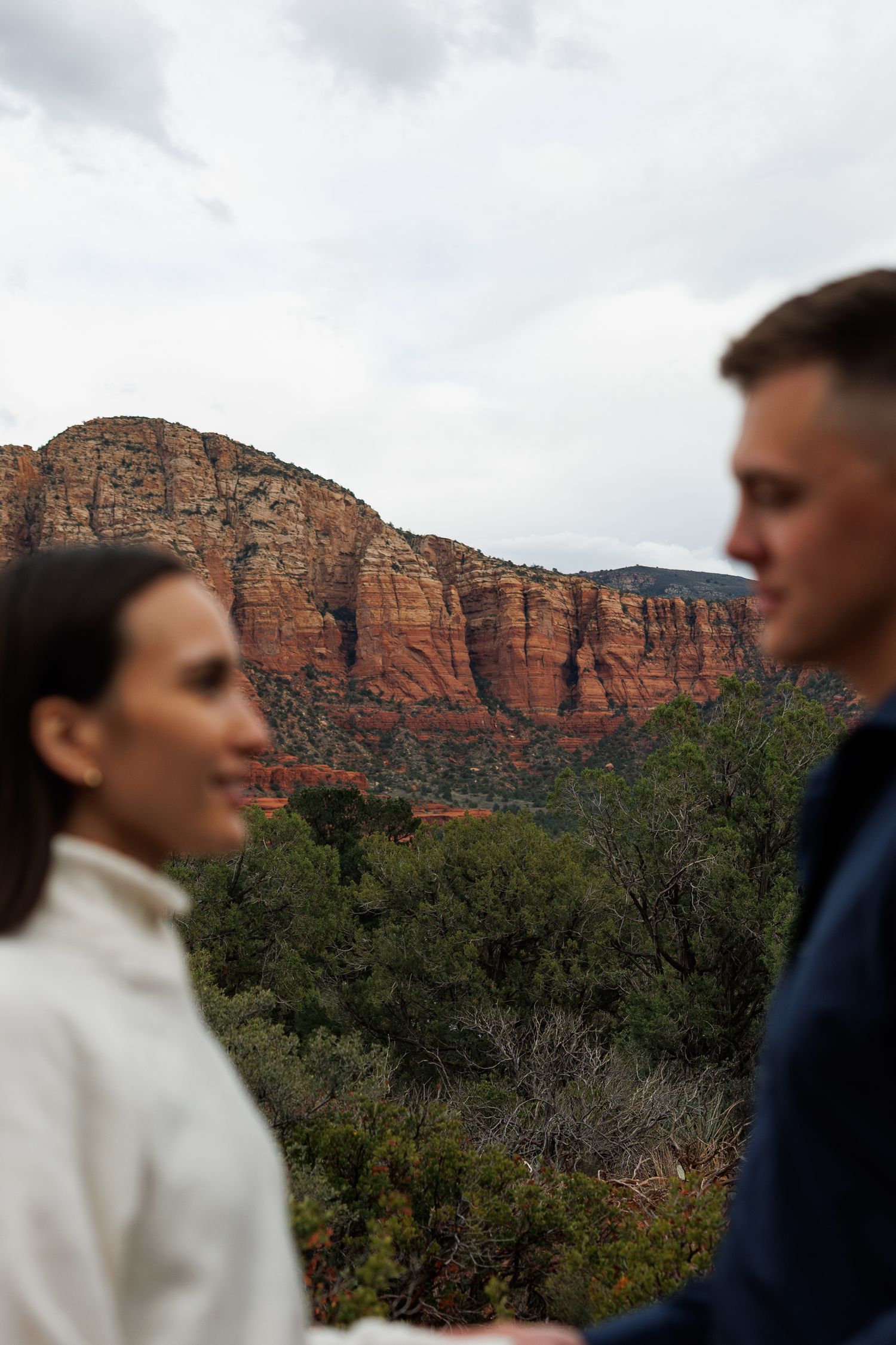 Couple holding hands with stunning Sedona red rock canyon landscape in background.