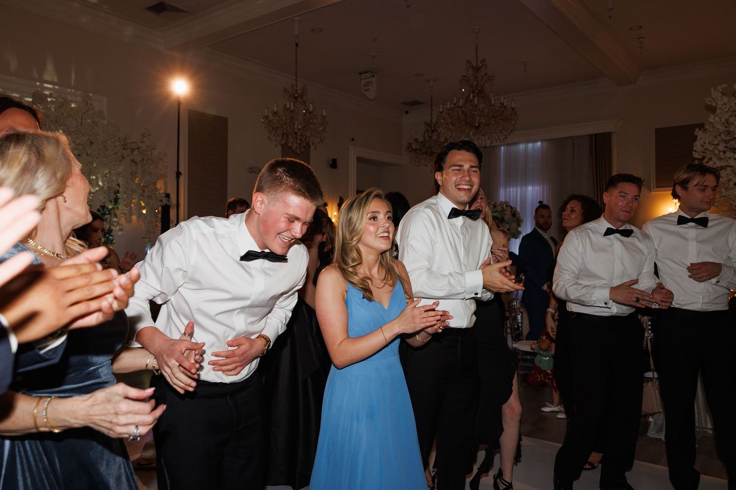Guests in formal attire dance and celebrate joyfully on the wedding reception dance floor.