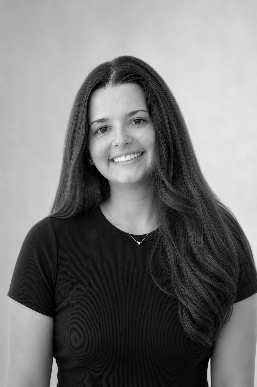 Black and white portrait of a smiling brunette woman in a black t-shirt against a light background.