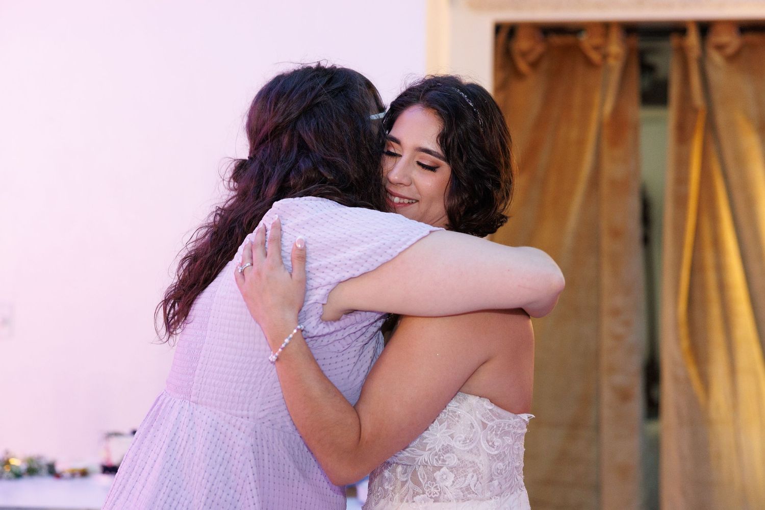 Bride and bridesmaid sharing an emotional hug at outdoor wedding celebration.