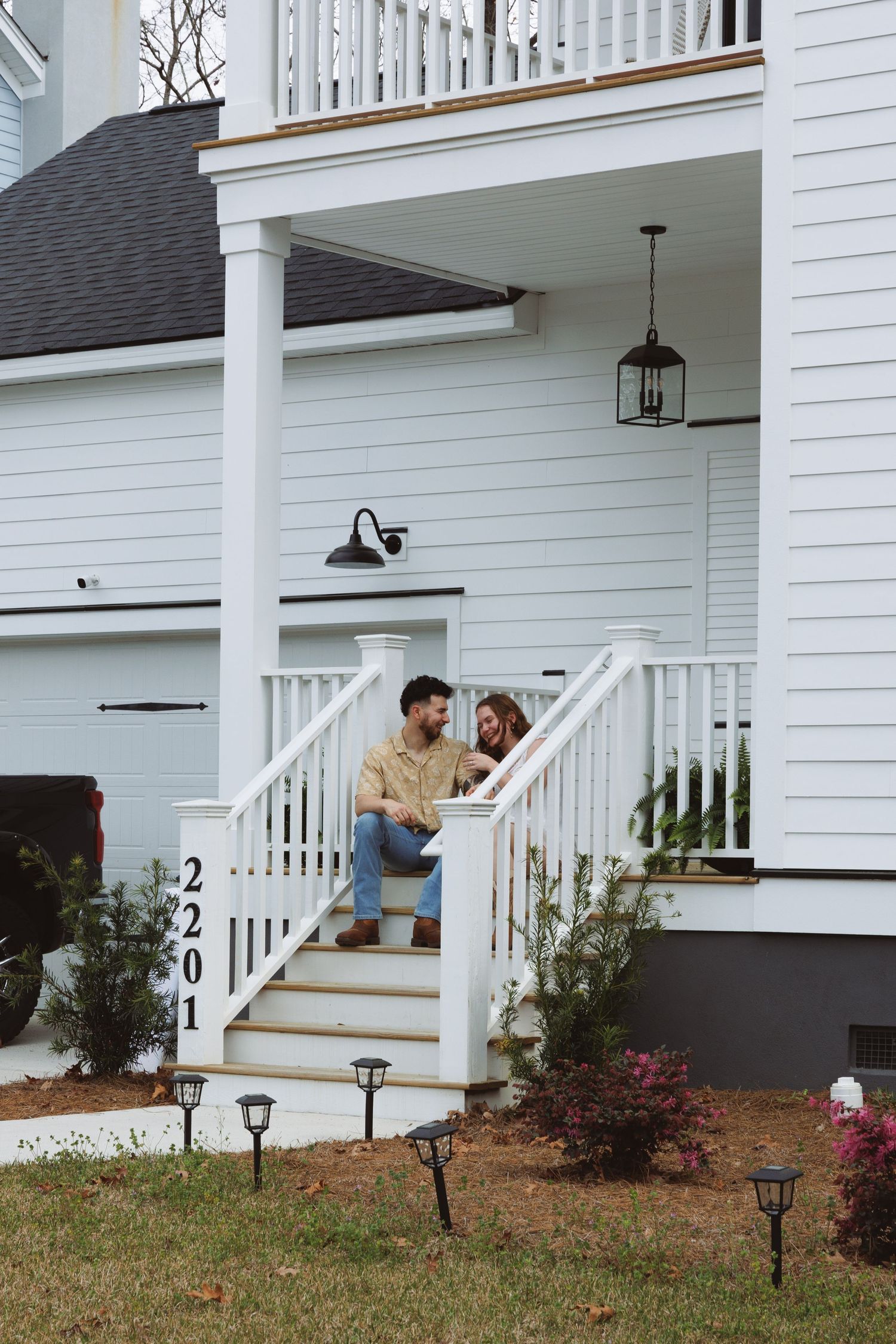 Couple sitting together on white front porch steps of a charming home with address 2201.