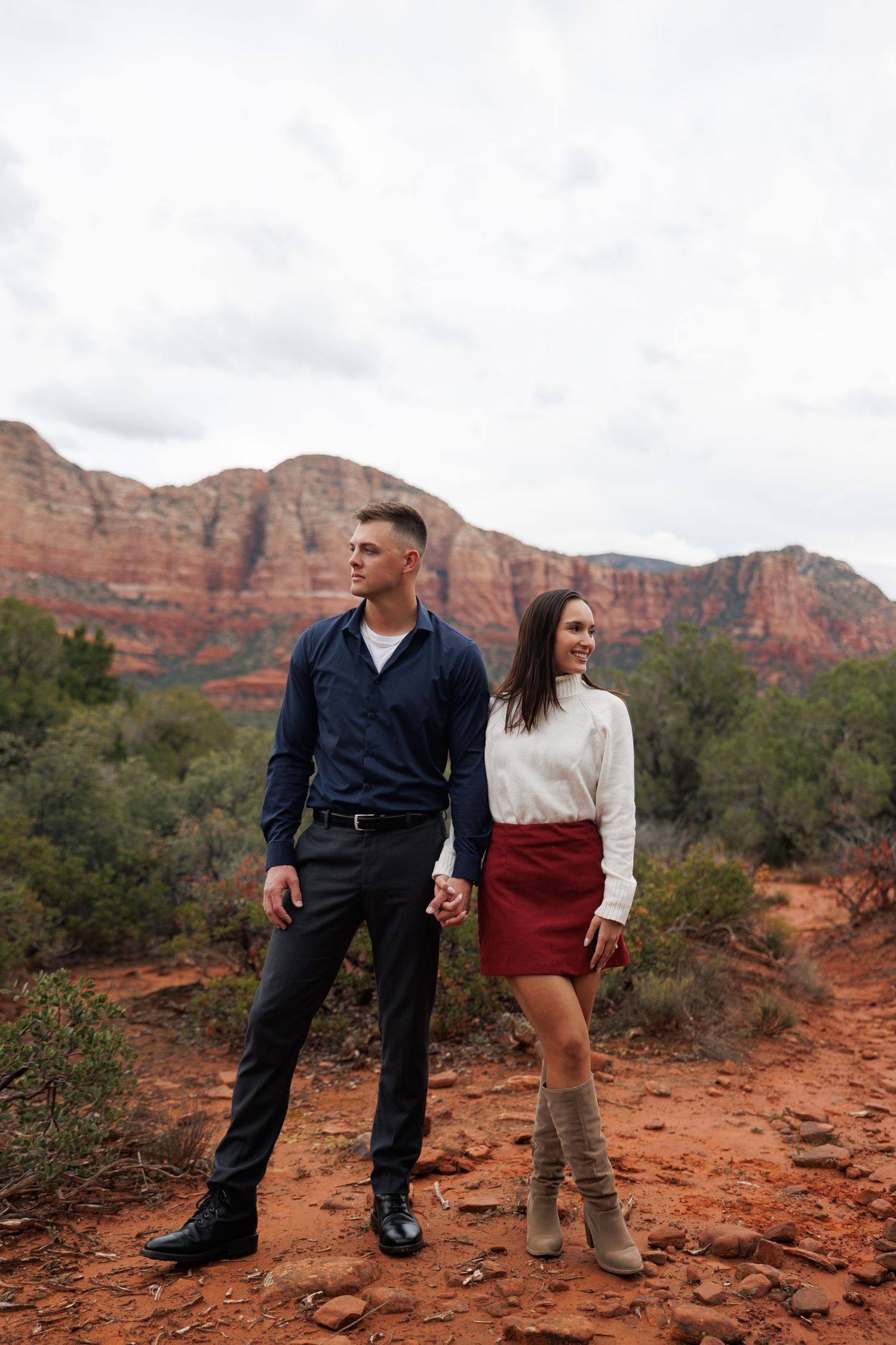 Couple holding hands in Sedona Arizona with red rock formations and desert landscape in background.