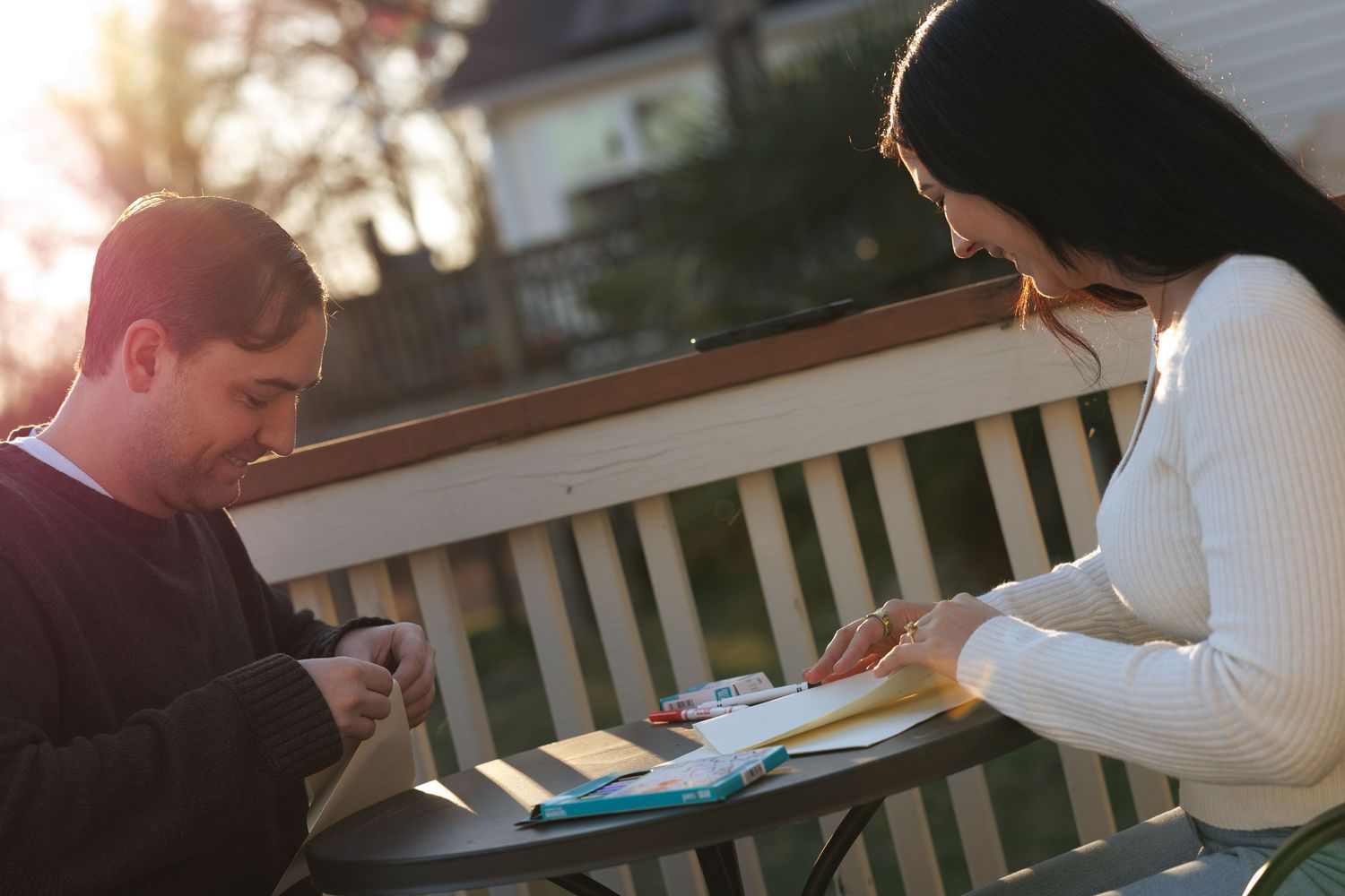 A man and woman sit at an outdoor table reviewing documents together in warm sunlight.