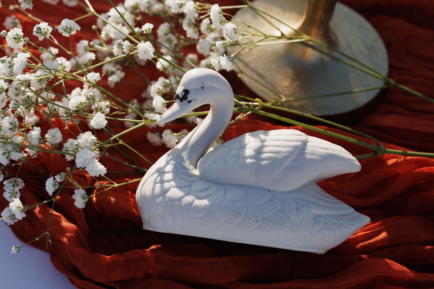 White ceramic swan figurine decoration with baby's breath flowers on red fabric at a wedding reception.