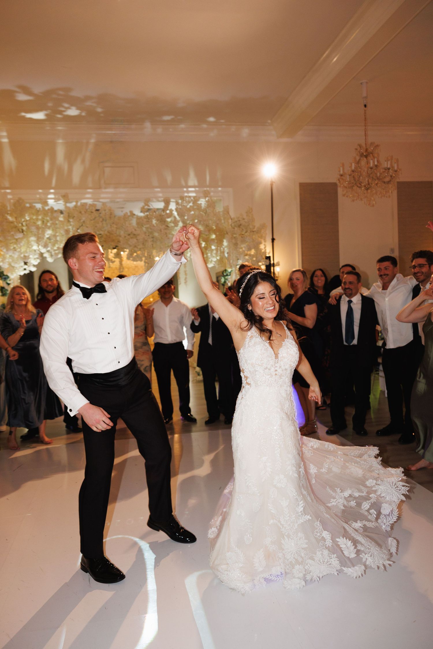 Joyful bride and groom spin together on white dance floor surrounded by guests at lively wedding reception at The Yorkmont in Charlotte, NC.