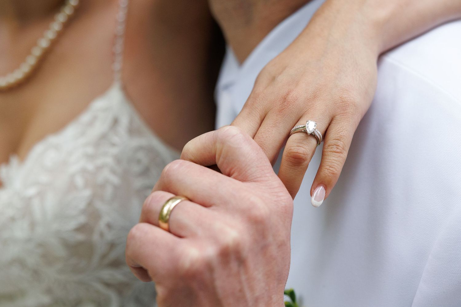 Close-up of newlyweds hands showing gold wedding band and diamond engagement ring on wedding day.