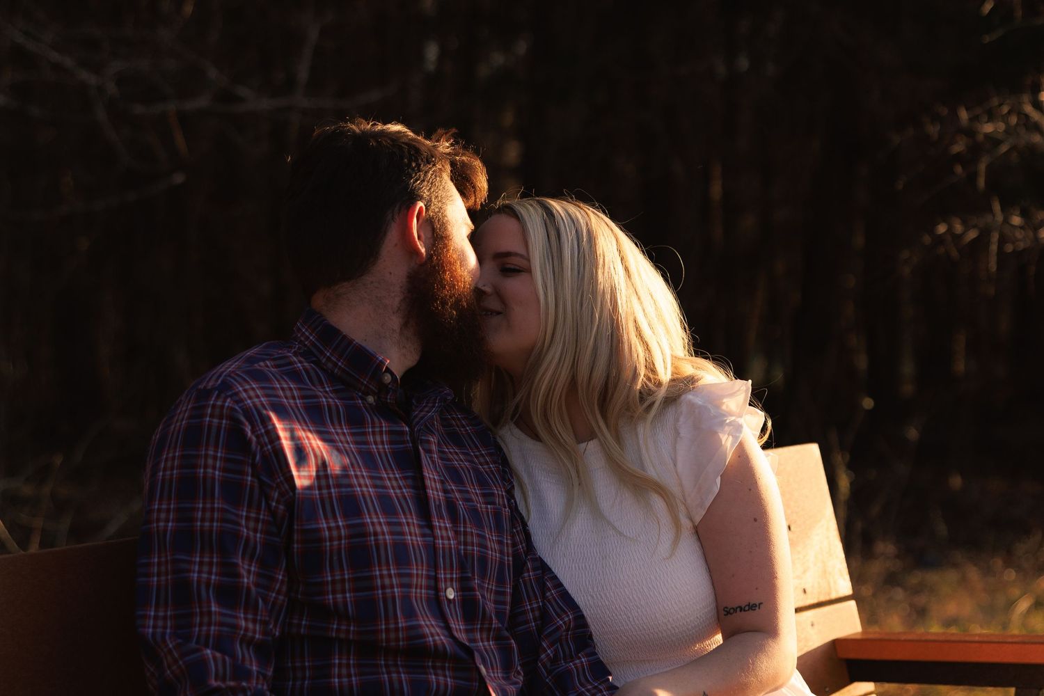 A couple shares a romantic moment on a wooden bench outdoors, bathed in warm golden sunset light.