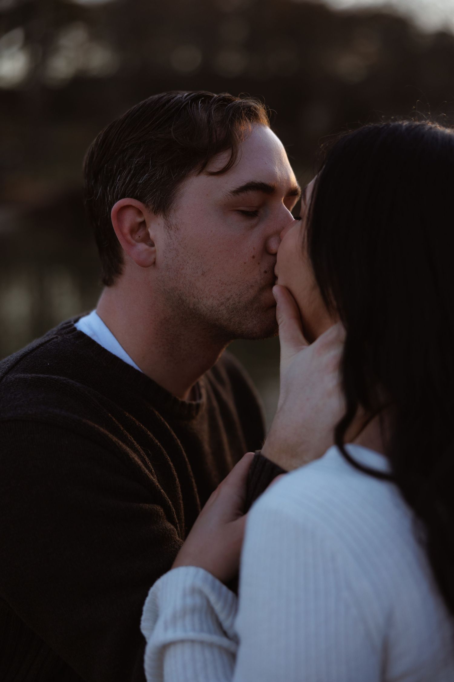 Couple sharing a tender kiss outdoors in soft evening light, man in dark sweater.