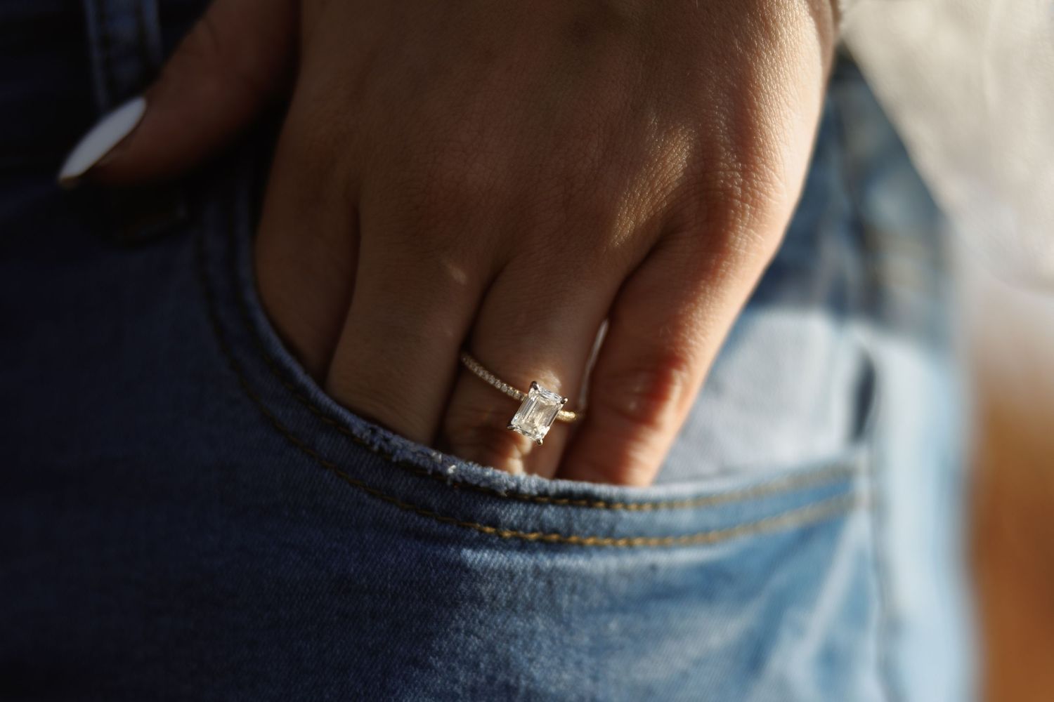 Close-up of a diamond solitaire engagement ring on a woman's finger tucked into a denim jeans pocket.