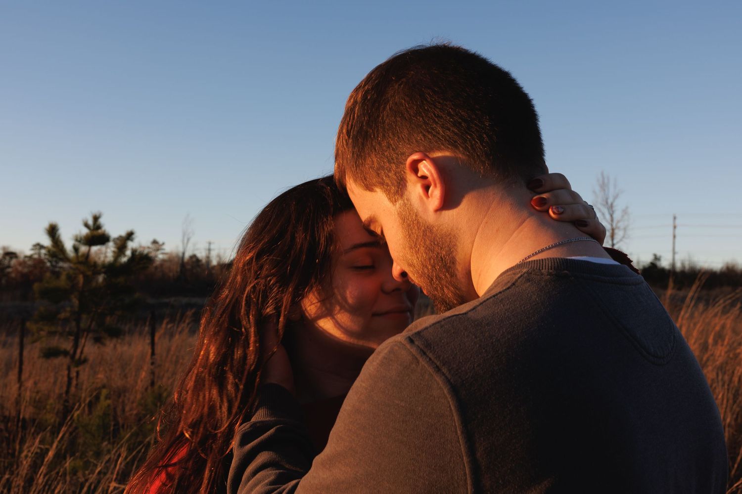 Couple sharing a tender romantic moment outdoors at golden hour in a field.