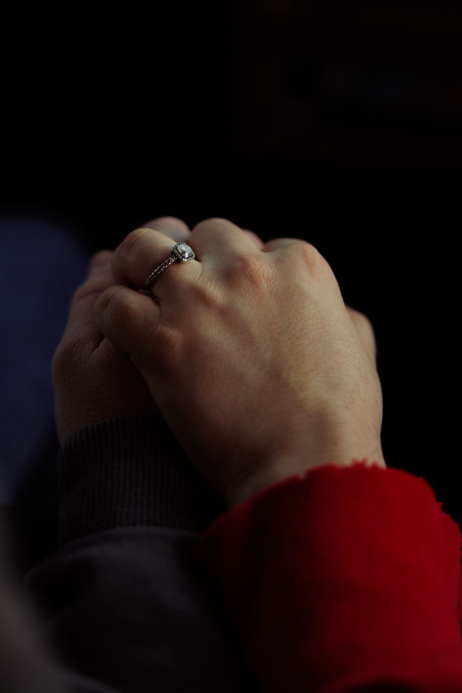 Two people hold hands closely, one wearing a sparkling diamond engagement ring on their finger.