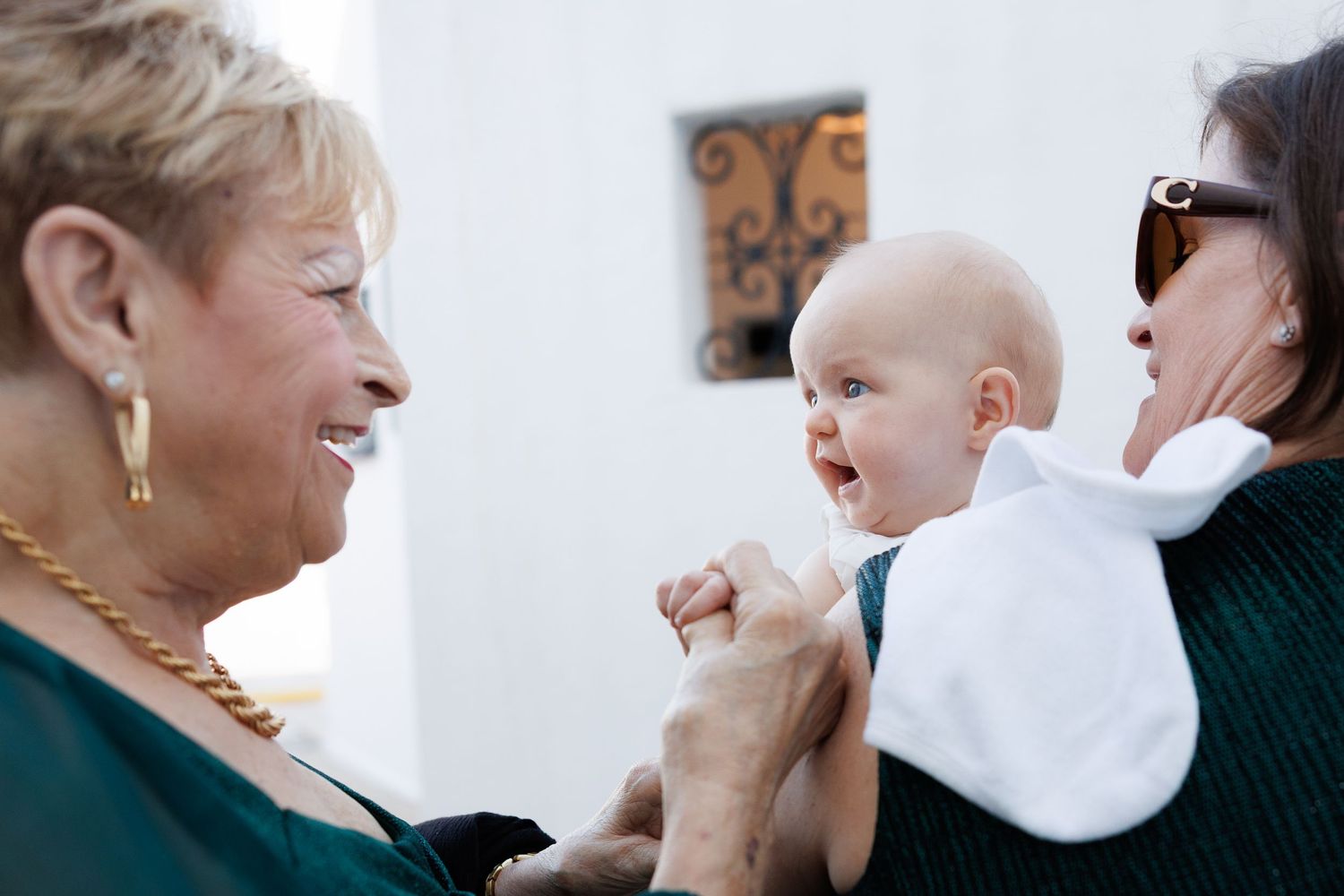 Two women smiling at an adorable baby during a family gathering, sharing a joyful moment together.