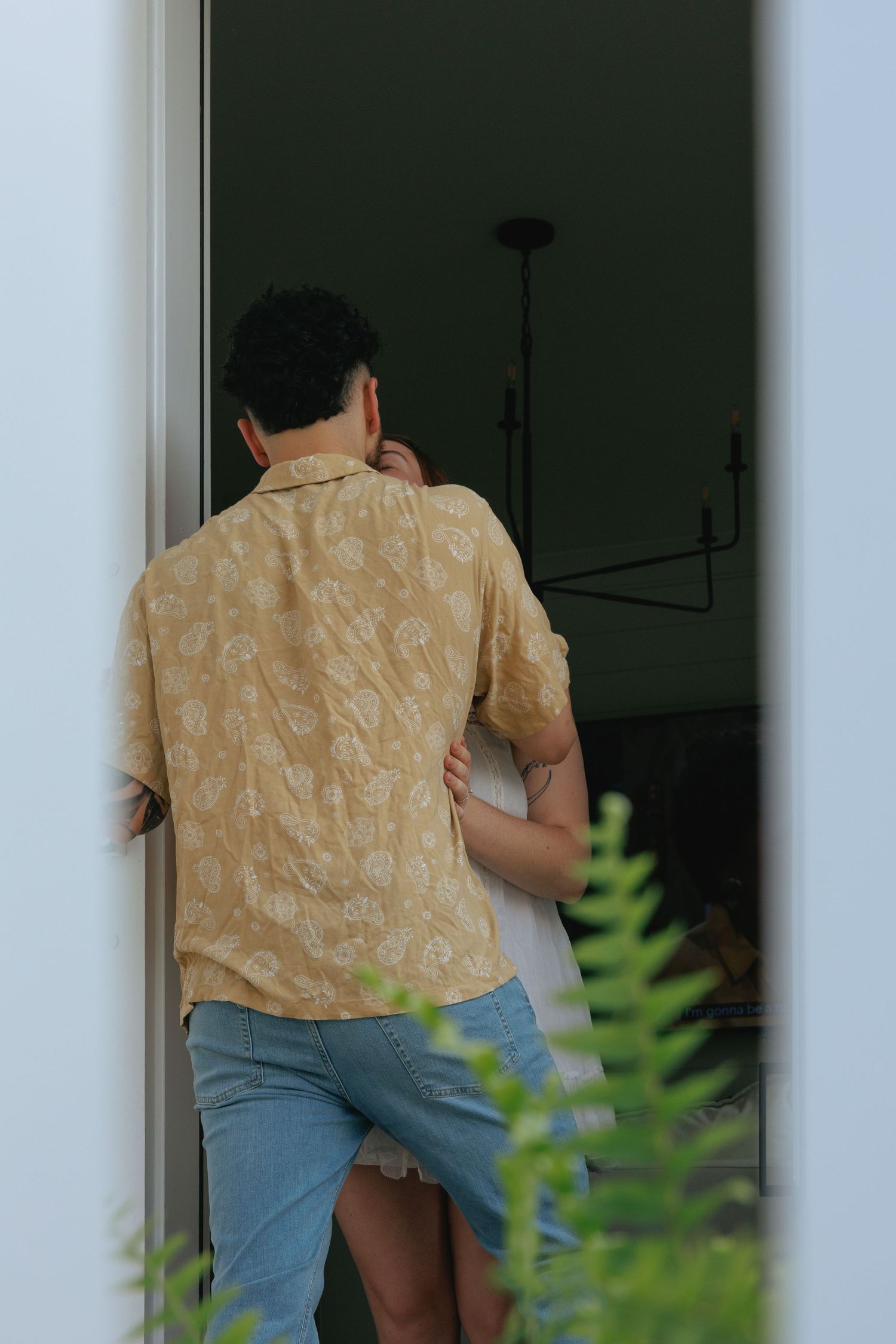 Couple embracing in a doorway, man wearing a yellow floral shirt and jeans.