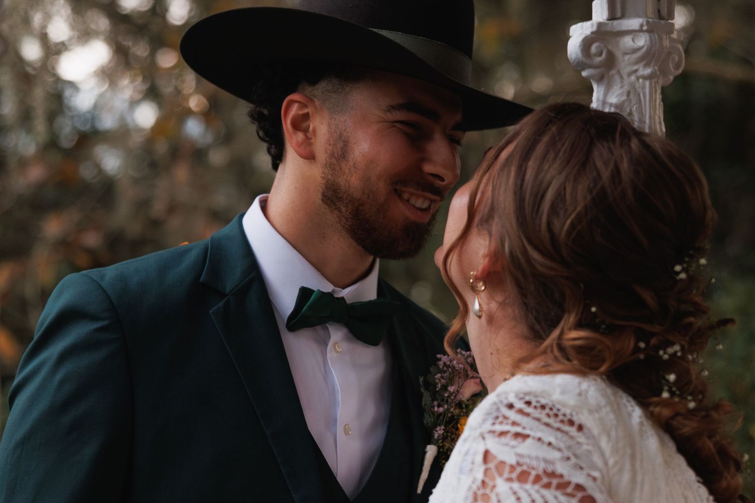 Groom in green suit and black cowboy hat smiling at bride during intimate wedding moment.