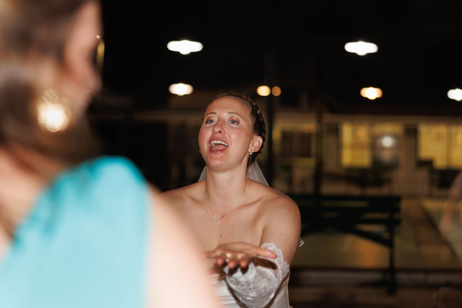 Woman in strapless dress gesturing while talking to another person in a dimly lit venue at night.
