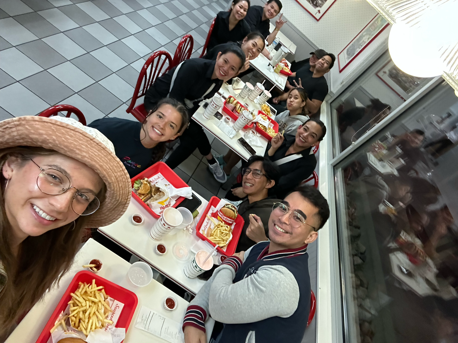 Large group of friends enjoying a meal together at In-N-Out Burger, smiling for a selfie photo.