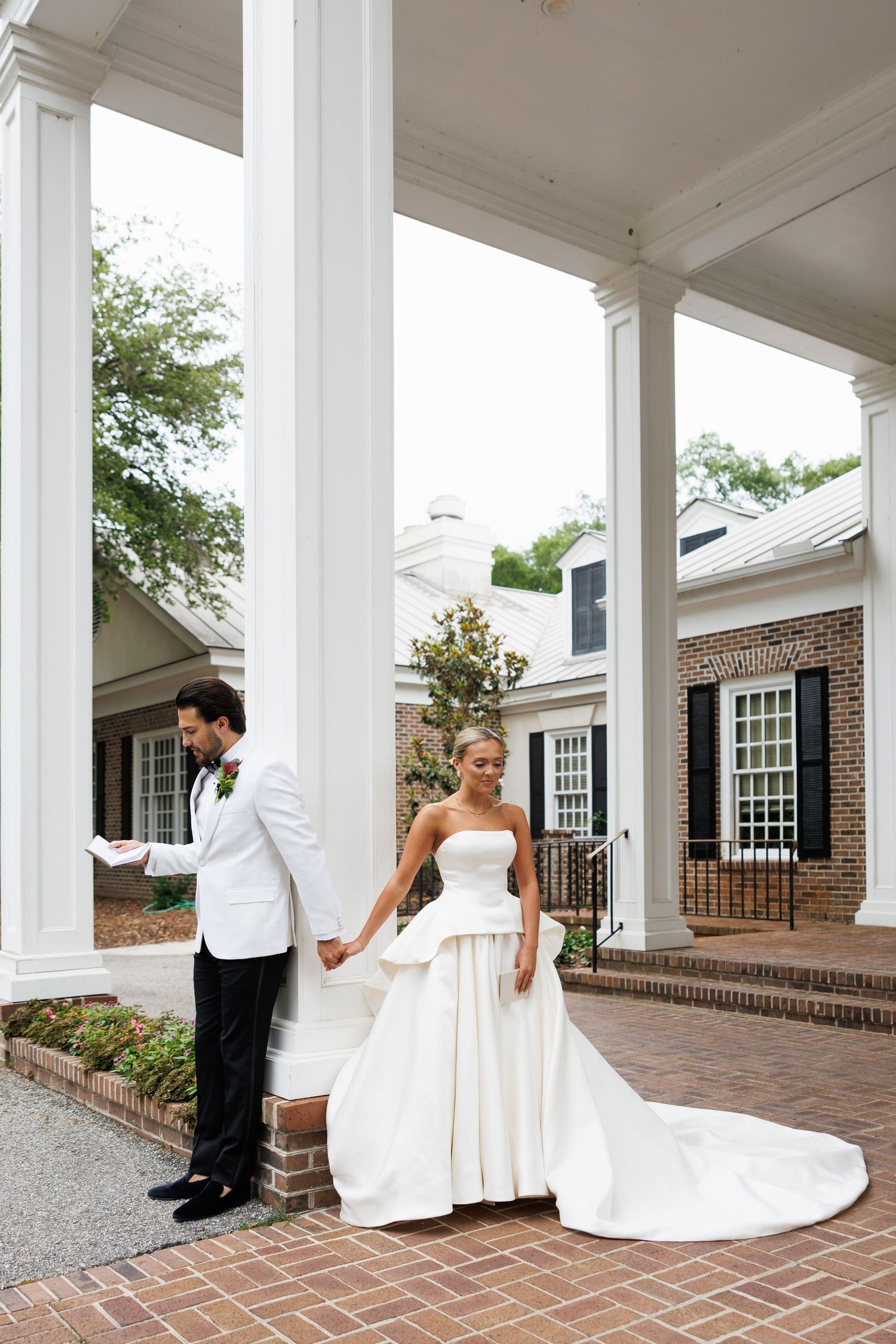 Bride in strapless ballgown and groom in white tuxedo share first look moment at elegant columned estate.