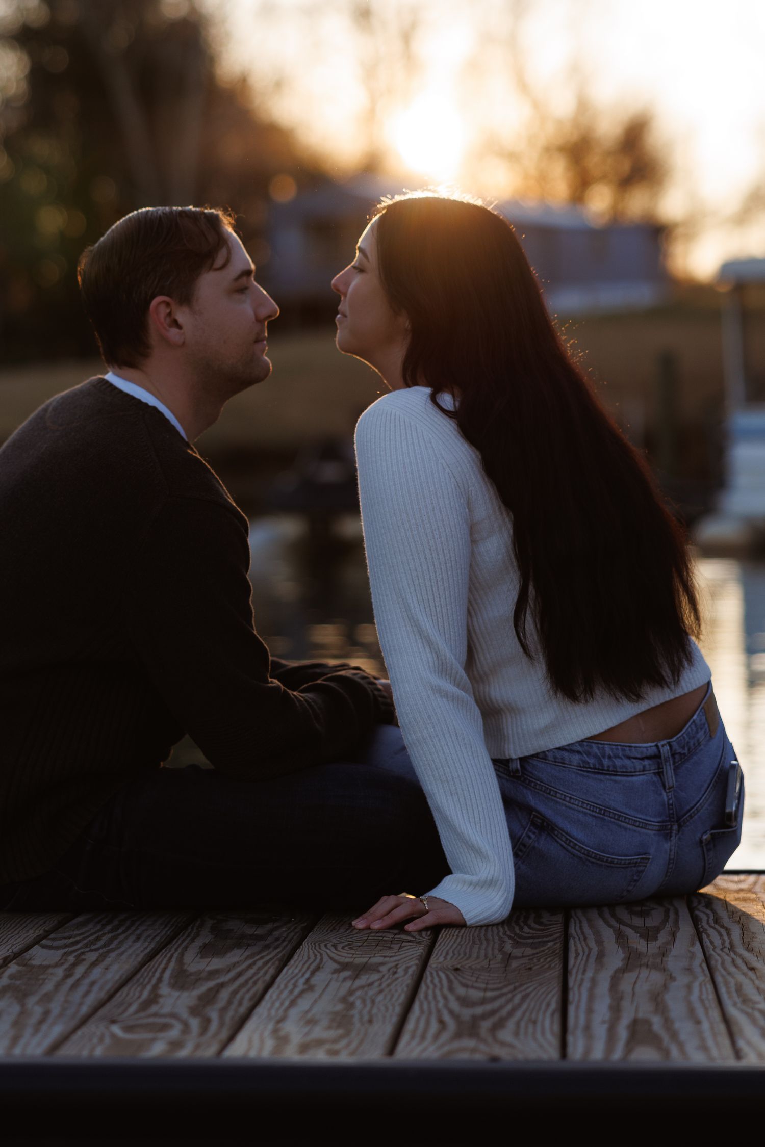 Romantic couple sitting close together on a wooden dock sharing an intimate moment at sunset.