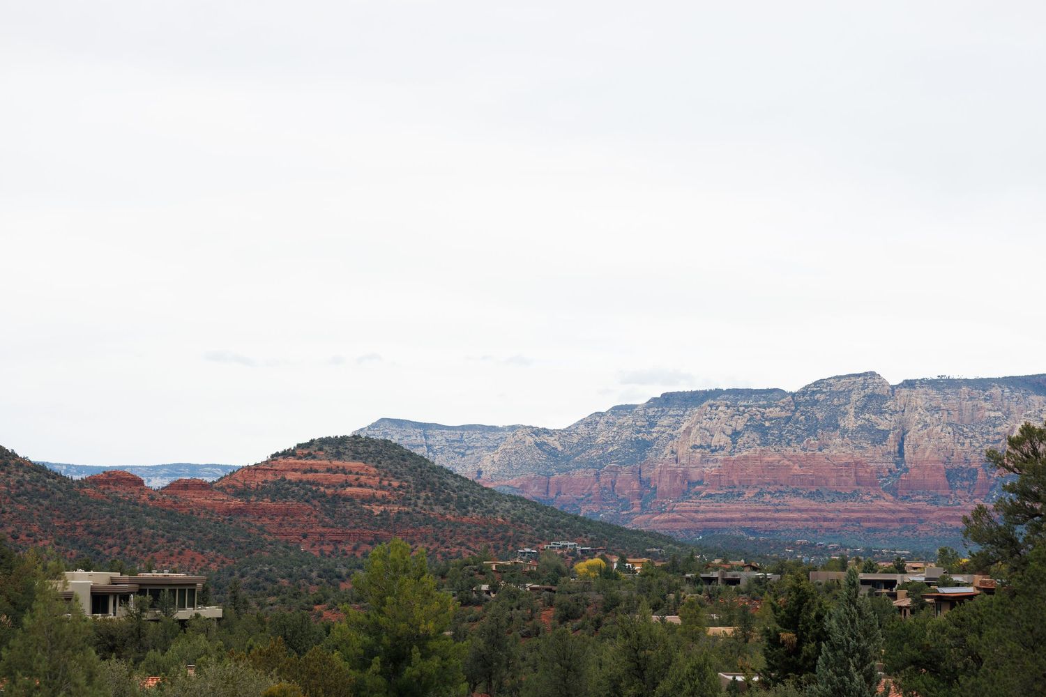 Red rock formations and lush green trees fill the landscape of Sedona, Arizona under a cloudy sky.