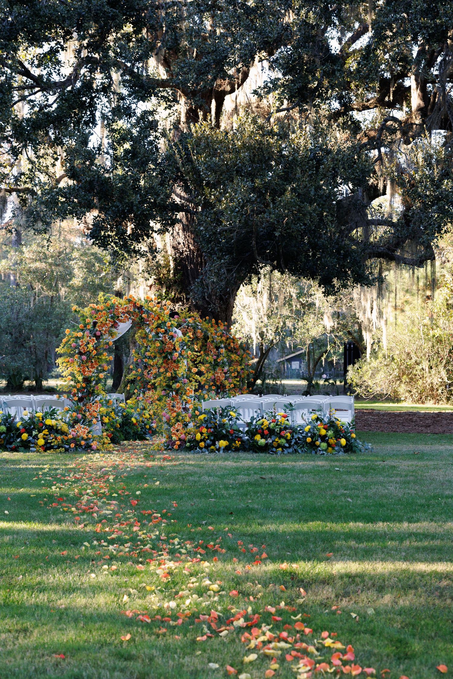 Colorful floral arch and garden arrangements beneath a large oak tree with Spanish moss in autumn.