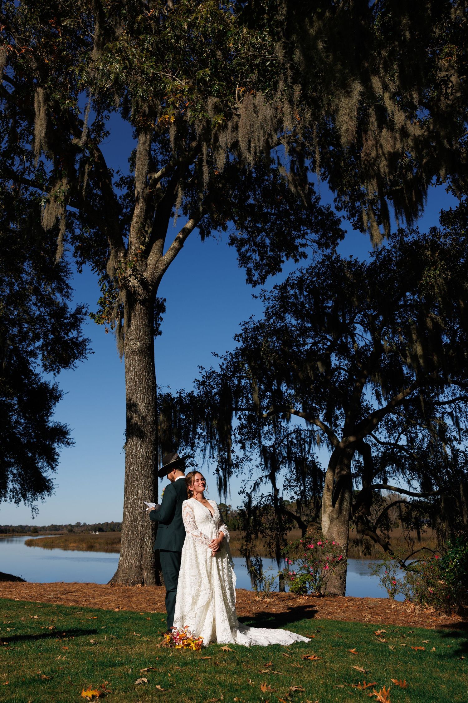 Bride and groom portrait under Spanish moss-draped oak trees beside a serene lake on wedding day.