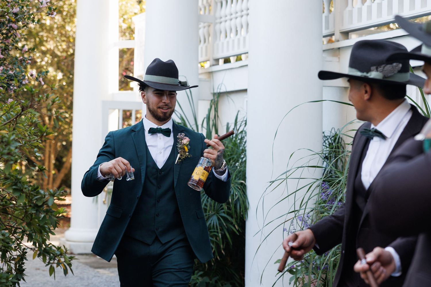 Two men in stylish suits and cowboy hats holding drinks outdoors at an elegant venue.