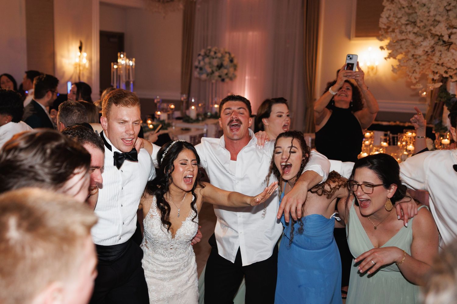 Bride and groom celebrate joyfully with wedding guests on the dance floor at reception.