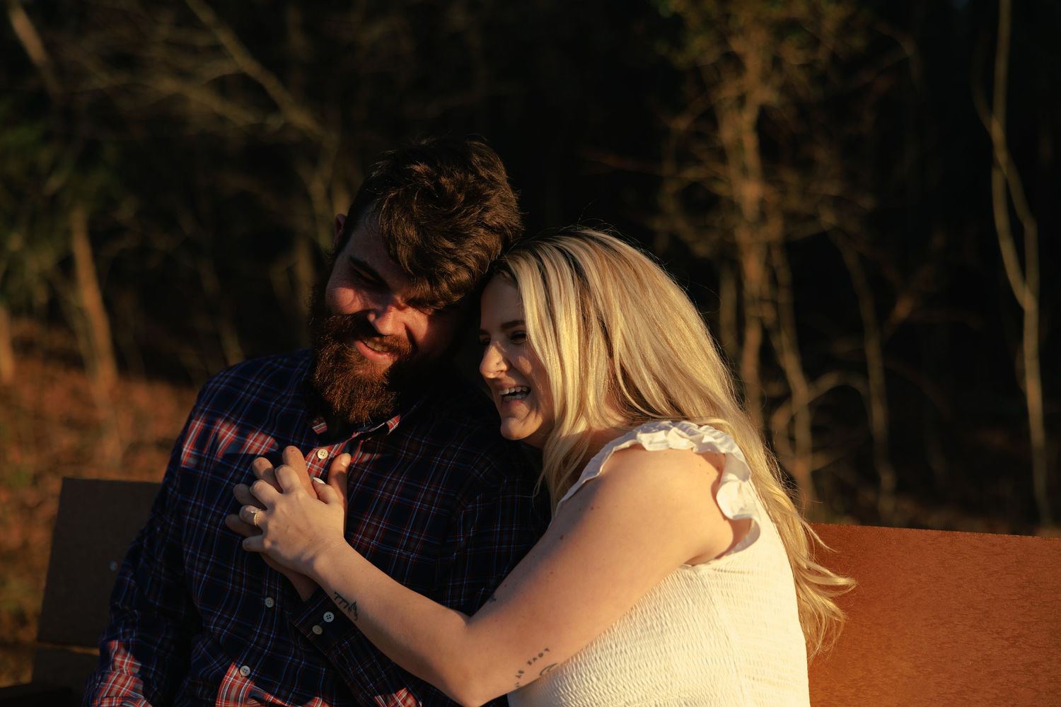 Bearded man and blonde woman sharing a joyful embrace at golden hour outdoors.