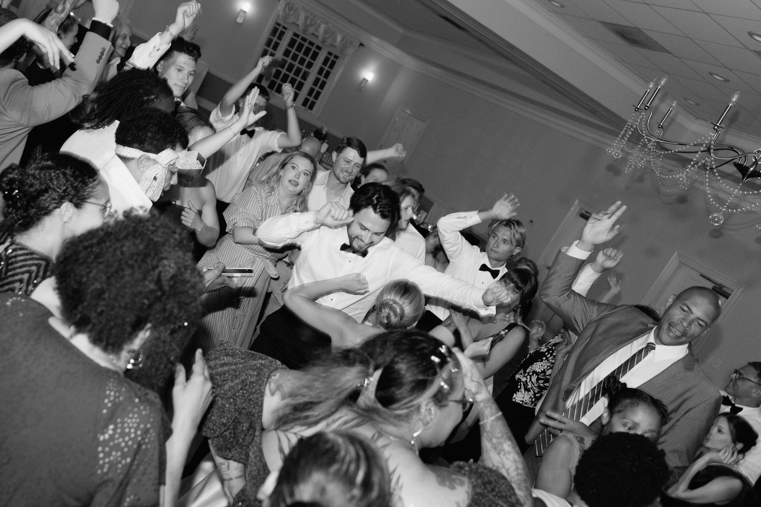 Black and white photo of a lively wedding reception dance floor filled with celebrating guests.