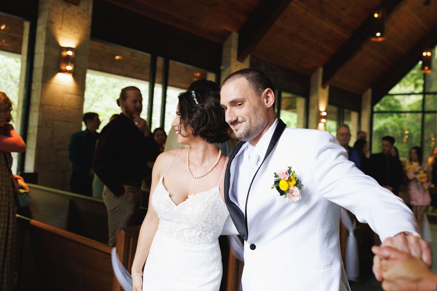Bride and groom share first dance at wedding reception, groom wearing white tuxedo with floral boutonniere.