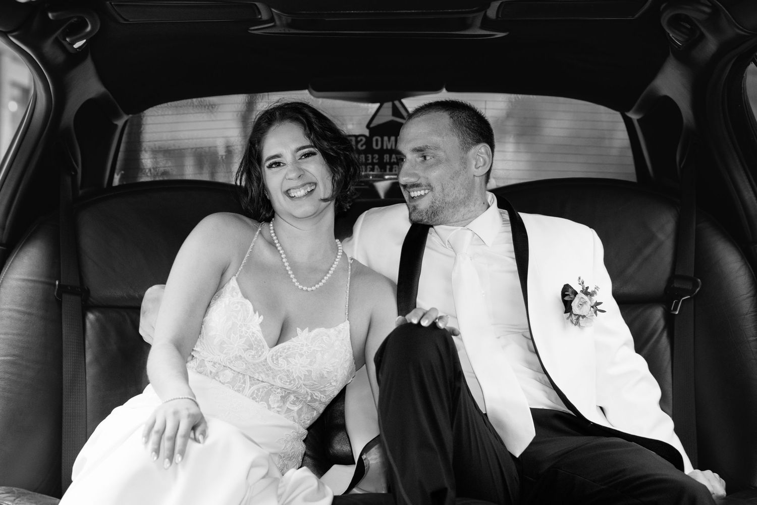 Black and white photo of smiling bride and groom sitting together in limousine after wedding.