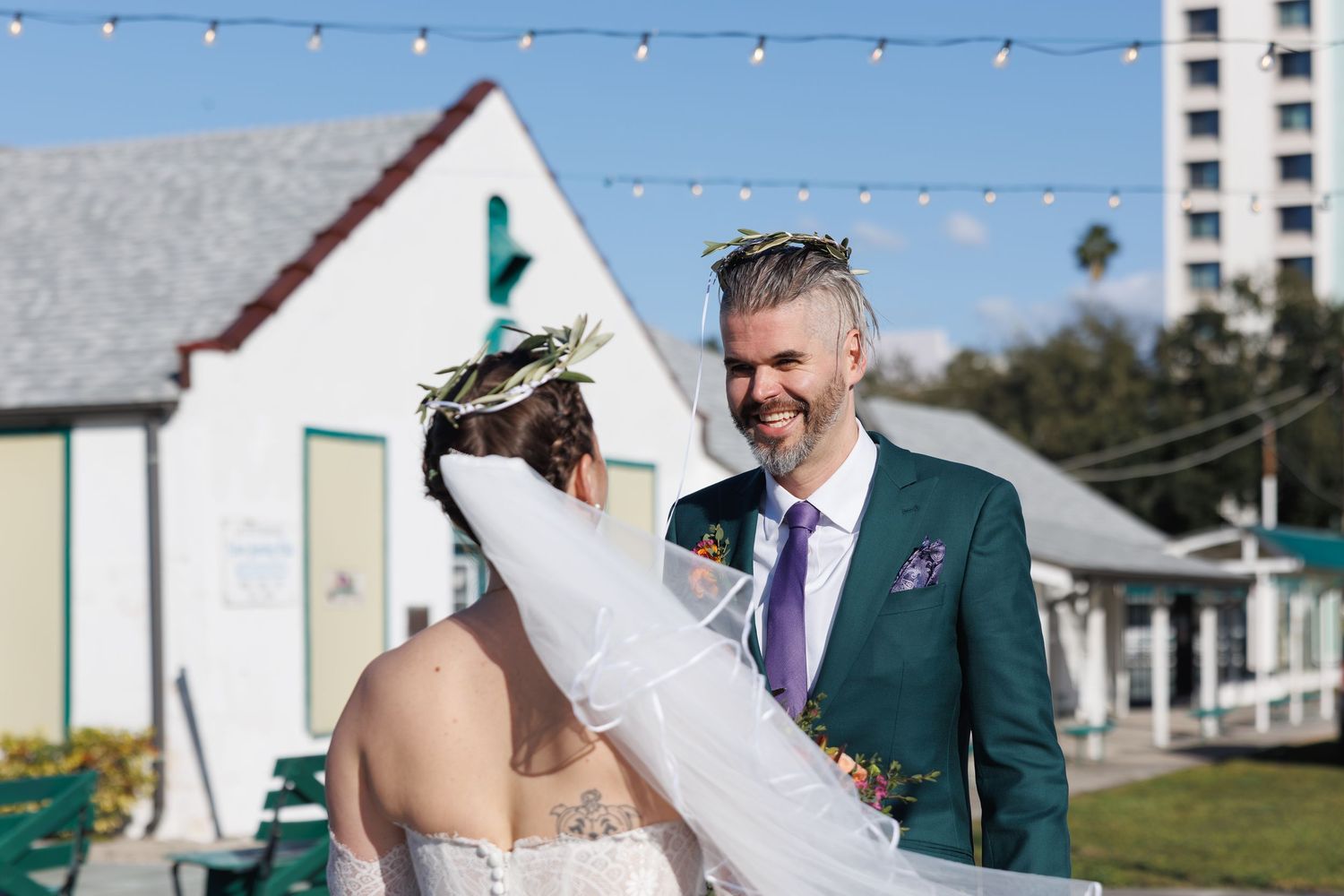 Newlywed couple sharing a romantic moment outdoors, groom in teal suit and bride in floral crown.