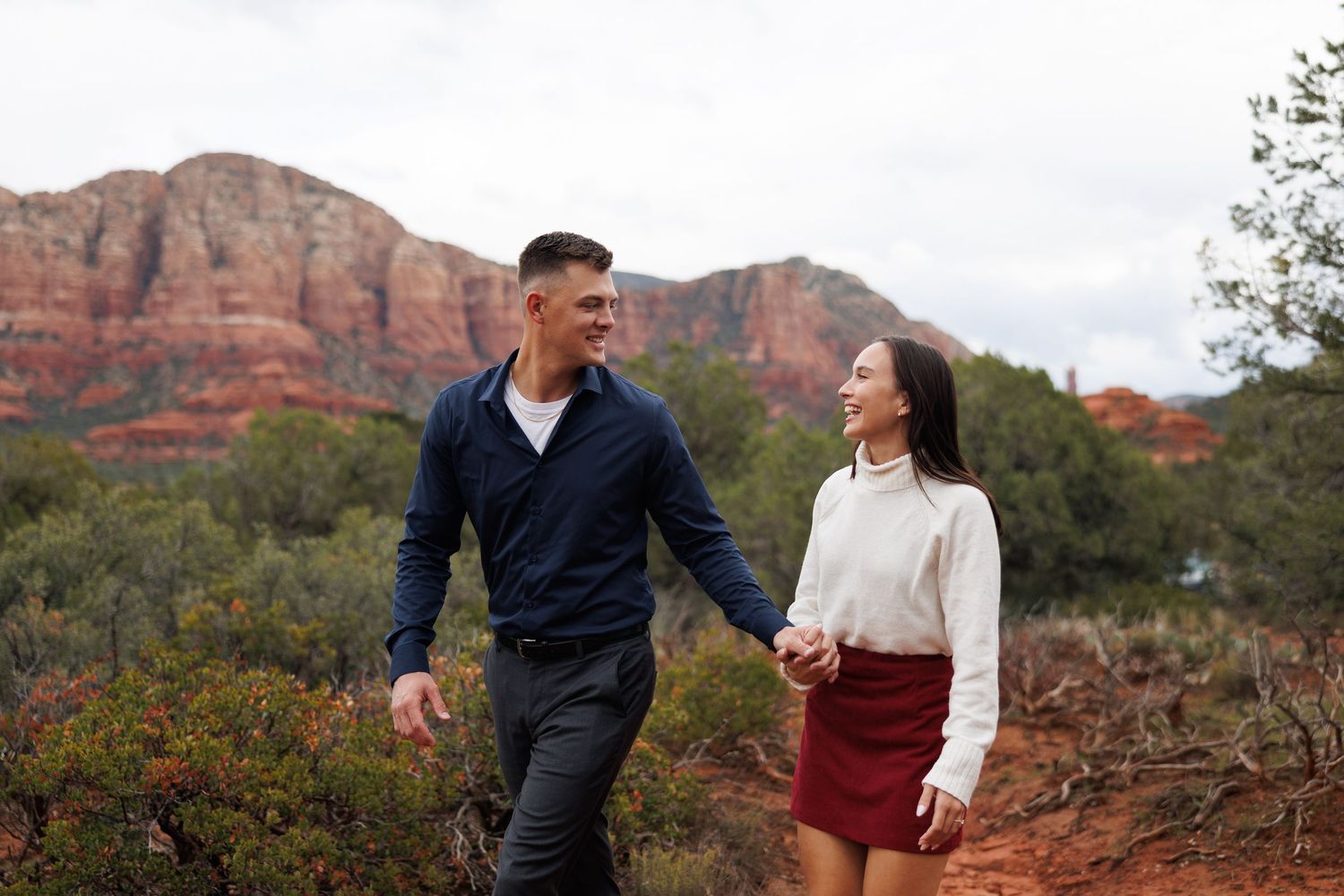 Couple holding hands walking on a trail with red rock formations in Sedona, Arizona.