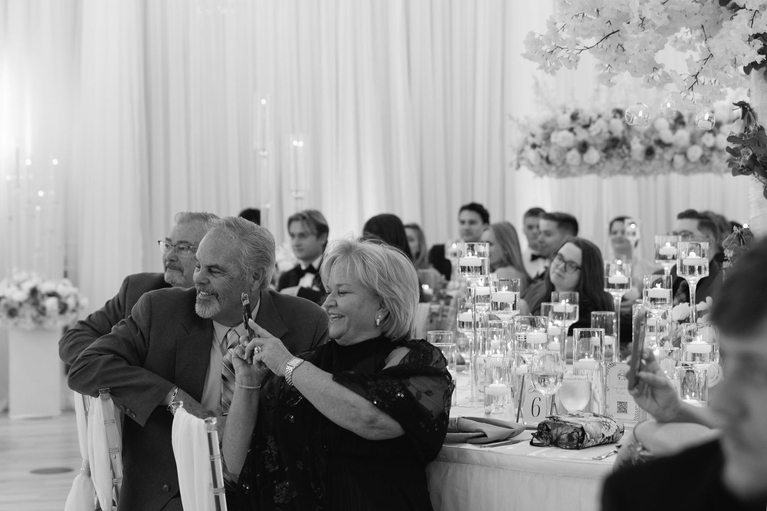 Wedding guests laugh and celebrate during reception speeches at elegantly decorated venue.