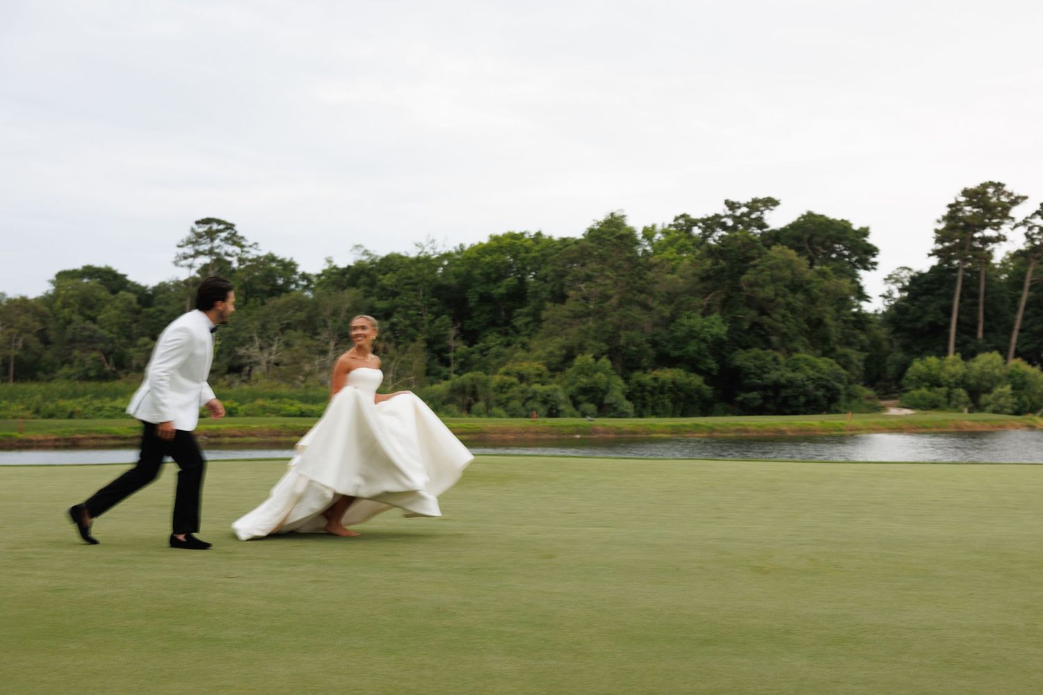 Bride and groom walking across a lush green golf course on their wedding day.