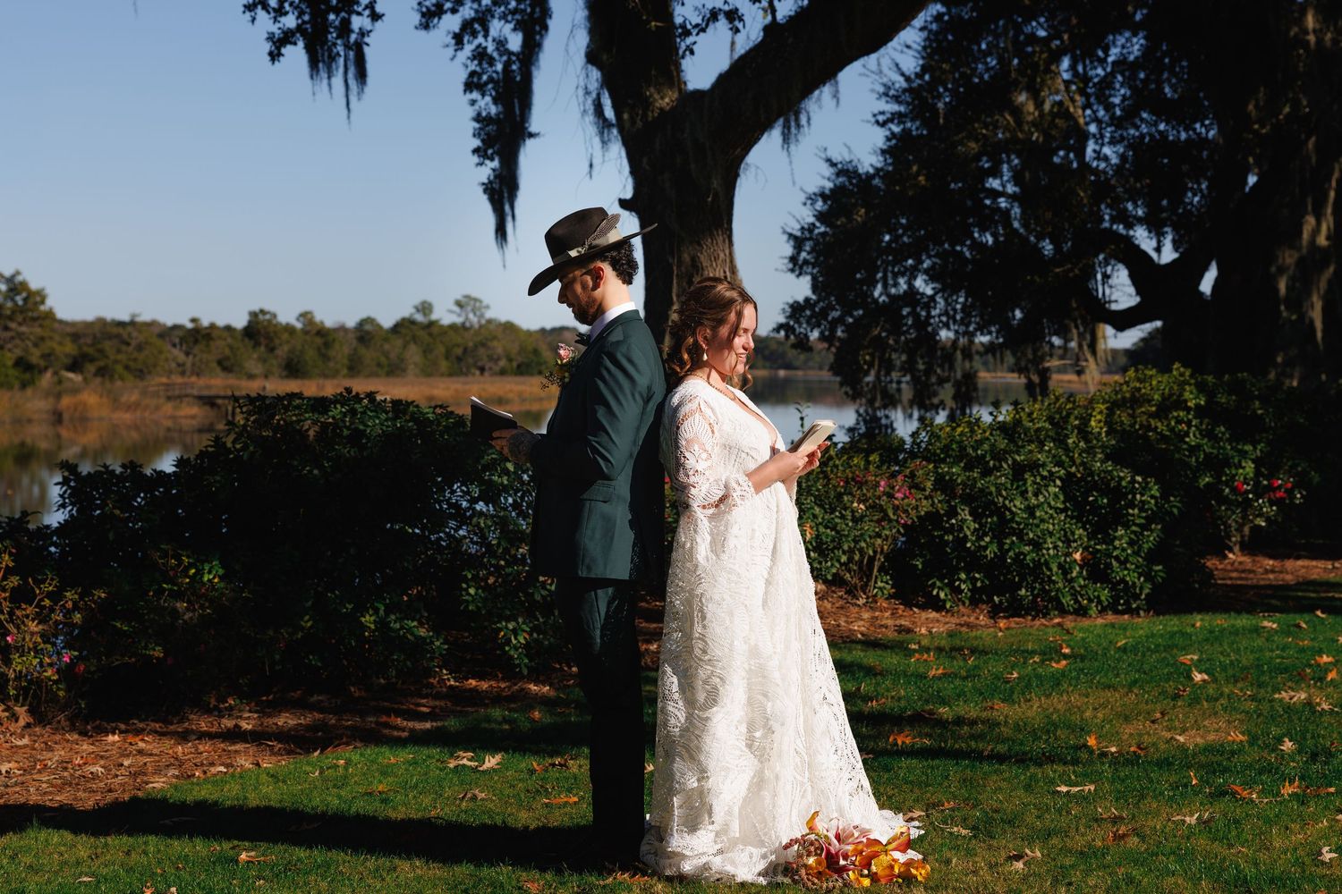 Bride and groom share a first look moment outdoors near a scenic lake surrounded by moss-draped oak trees.