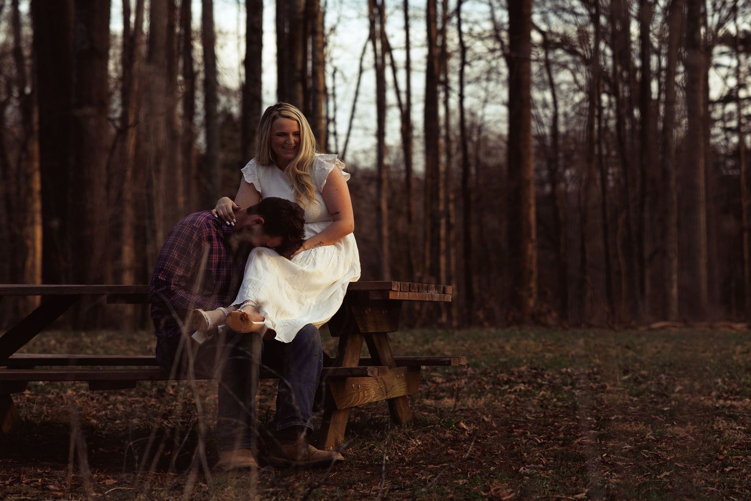 Couple sharing intimate moment on wooden steps in forest, woman in white dress and man in plaid shirt.