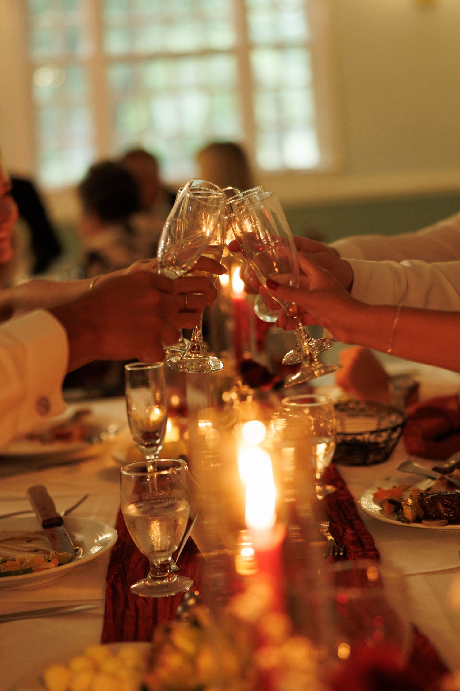 Wedding guests clink crystal wine glasses in a candlelit toast at an elegant reception dinner table.