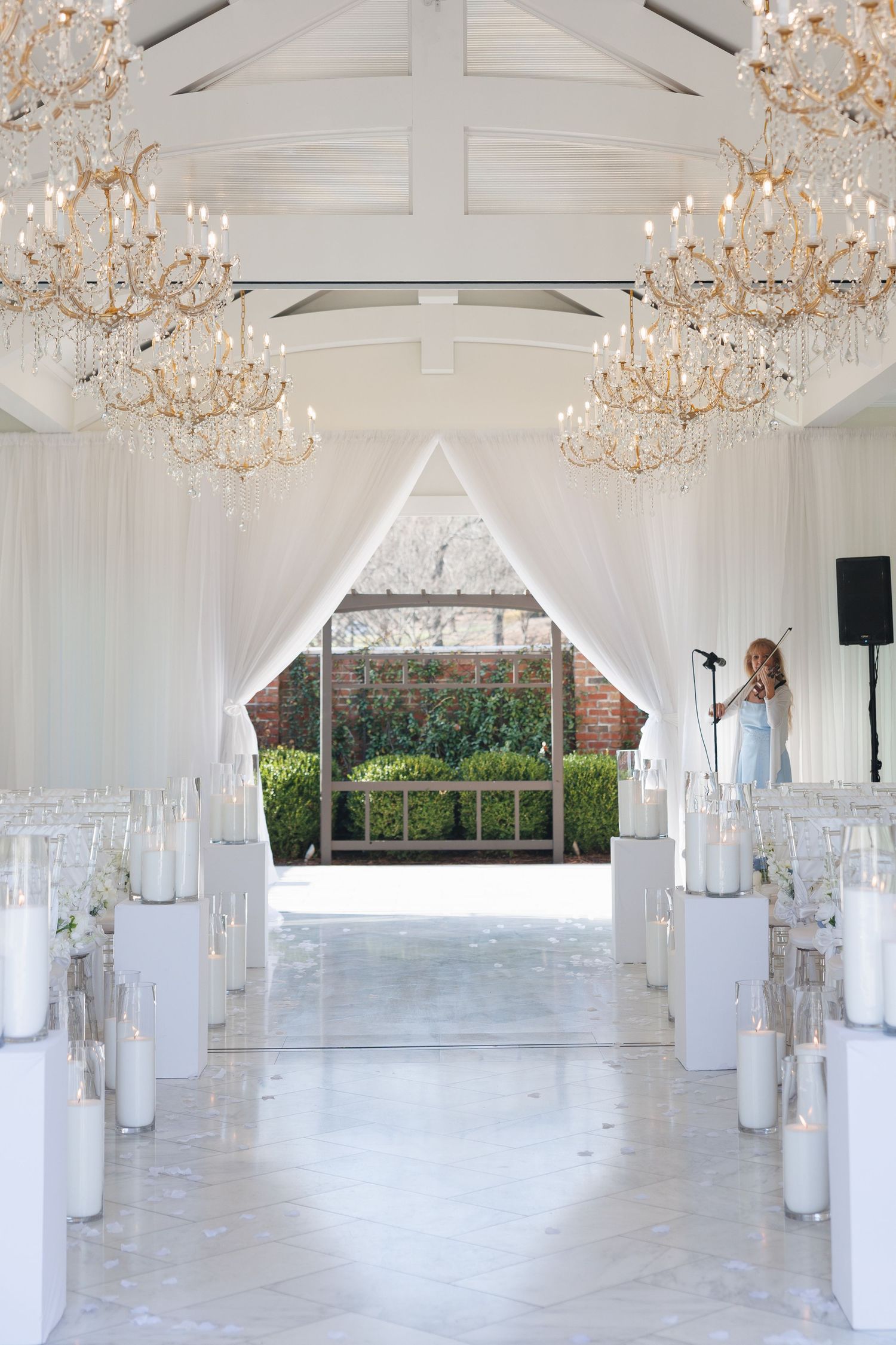 A stunning all-white wedding ceremony hall with crystal chandeliers, candle pedestals, and draped fabric aisle at The Yorkmont in NC.