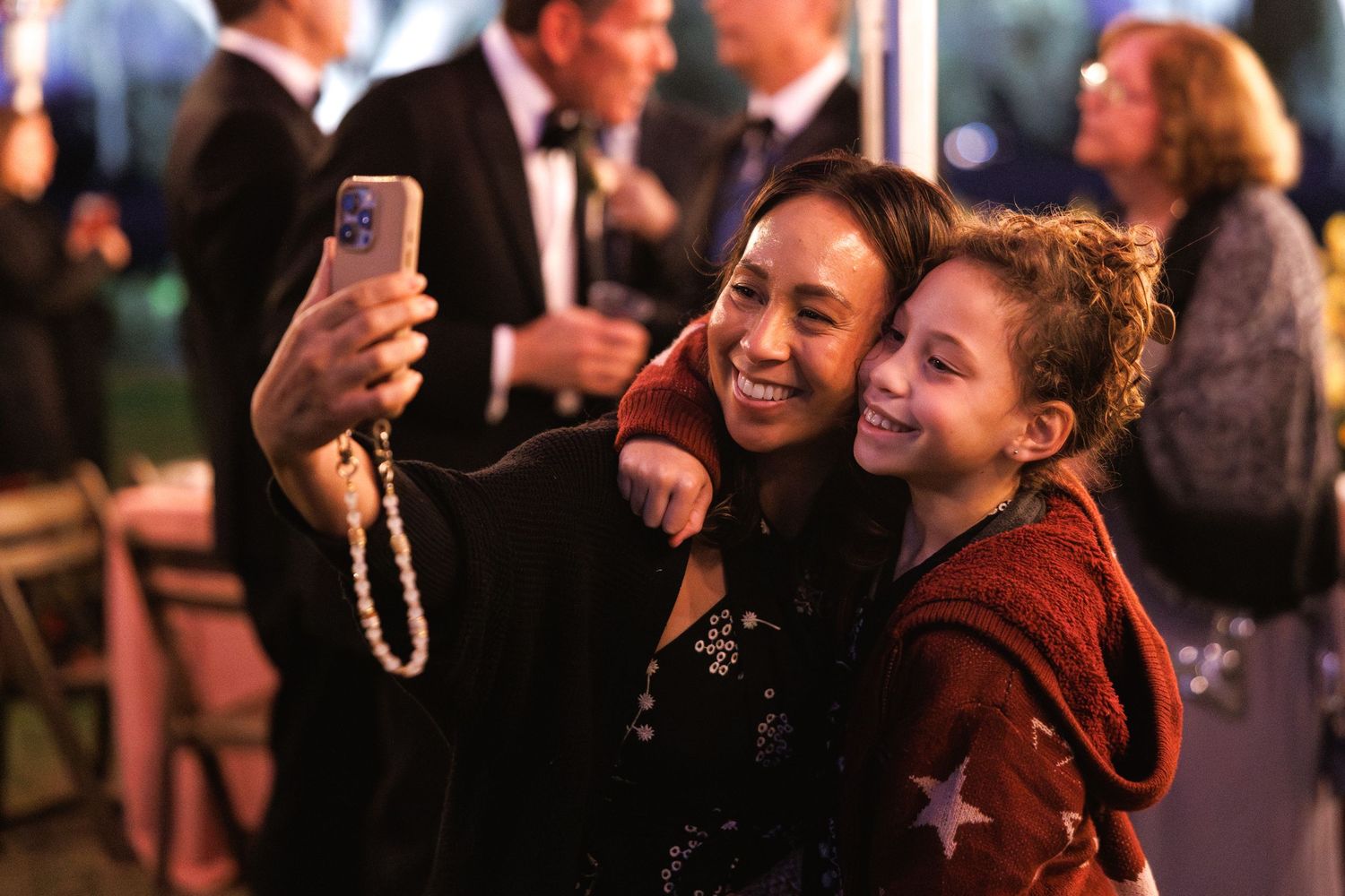 Woman and young girl smiling together taking a selfie at an elegant evening celebration event.