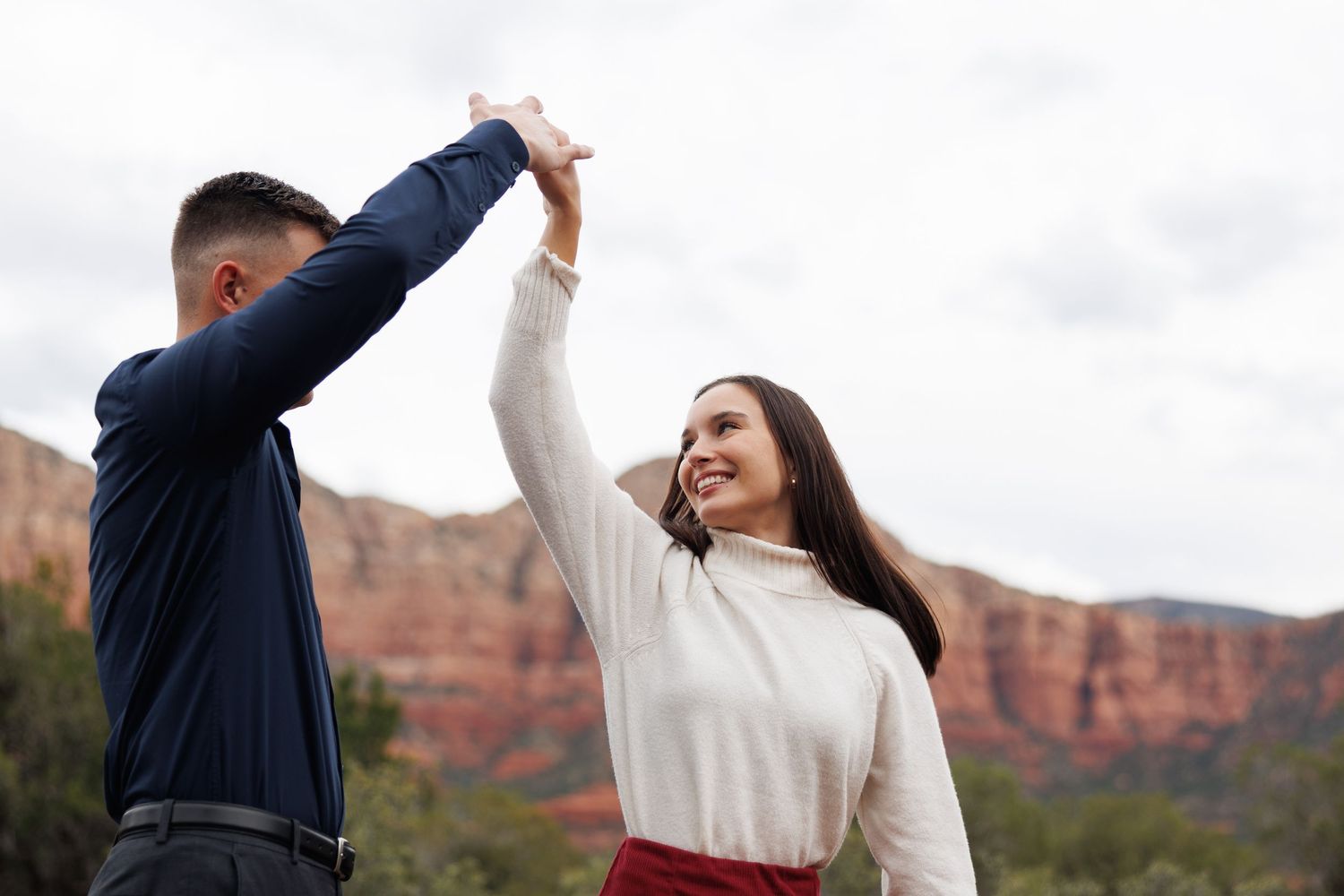 Couple dancing and spinning hands raised with Sedona red rock mountains behind them.