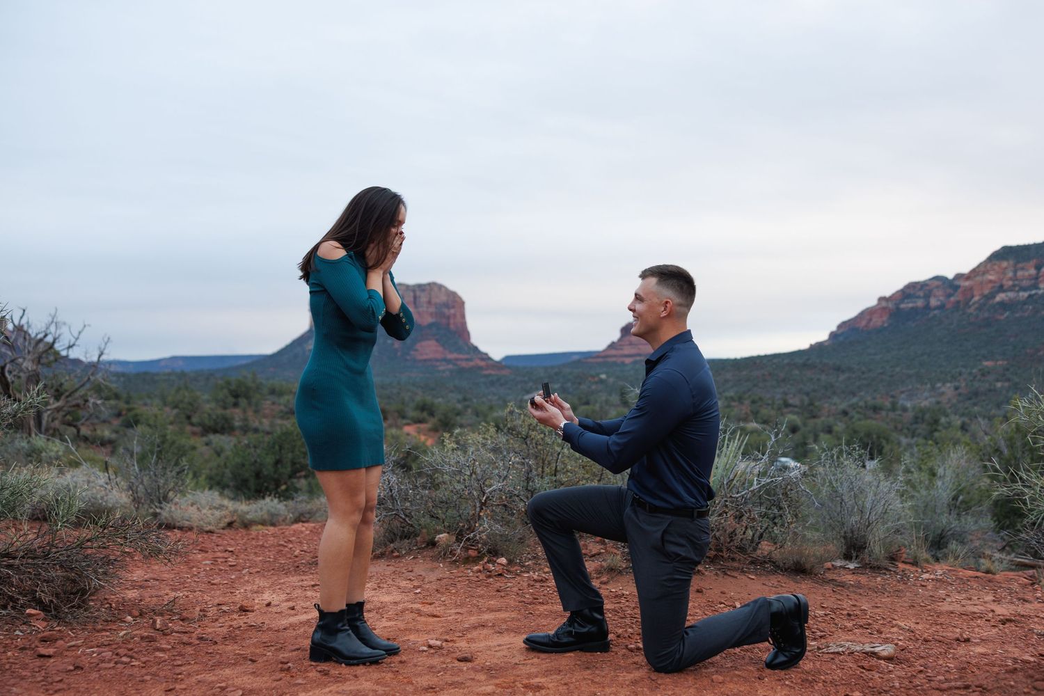 Man proposes to woman on one knee in Sedona Arizona red rock desert landscape at dusk.